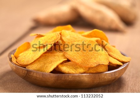 Crispy Peruvian sweet potato chips on wooden plate with sweet potatoes in the back (Selective Focus, Focus on the middle of the sweet potato chip in the front)
