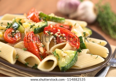 Vegetarian penne pasta dish with baked zucchini and tomato spiced with thyme and garlic (Selective Focus, Focus on the front of the tomato slice on the top of the dish)