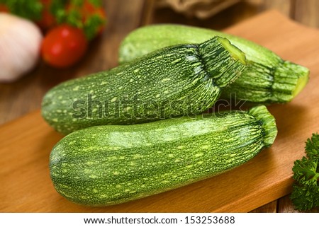 Raw zucchini on wooden board with other ingredients in the back (Selective Focus, Focus on the tip of the two zucchinis in the front)