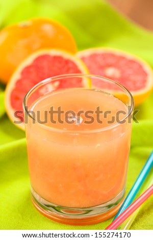Freshly squeezed juice of the pink-fleshed grapefruit with drinking straws on the side and grapefruits in the back on green fabric (Selective Focus, Focus on the bubble on the middle of the juice)