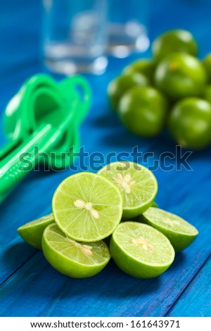 Lime halves on blue wood with squeezer and glasses in the back (Selective Focus, Focus on the lime half on the top)