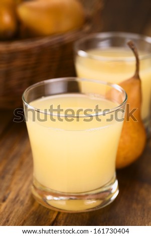 Pear juice in glass with Bosc pear in the back on dark wood (Selective Focus, Focus on the front rim of the glass)