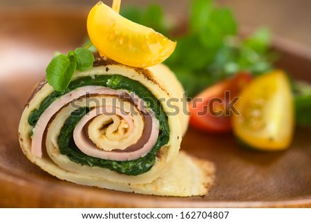 Crepe roll as finger food filled with spinach and ham garnished with cherry tomato and watercress served on wooden plate (Selective Focus, Focus on the upper part of the crepe roll)