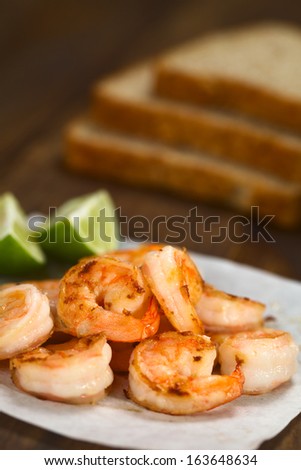 Fresh fried shrimps with lime wedges on sandwich paper with toast bread slices in the back (Selective Focus, Focus one third into the shrimps)