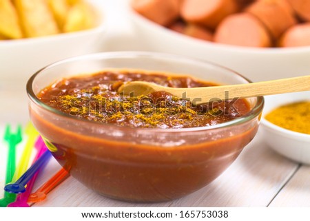Curry ketchup sauce made to dip fried sausages and French fries served in glass bowl with wooden spoon, colorful plastic party forks on the side (Selective Focus, Focus one third into the sauce)