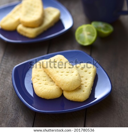 Homebaked shortbread biscuits on small plates with cup of tea in the back (Selective Focus, Focus on the front of the upper shortbread)