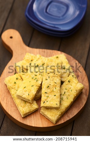 Fresh homemade garlic and cheese sticks made of a yeast dough served on wooden board, sprinkled with fresh thyme leaves (Selective Focus, Focus one third into the garlic sticks)