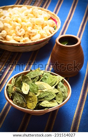 Dried coca leaves in bowl with fresh coca tea (mate de coca) and Bolivian snack Pasancalla (popped corn), photographed with natural light (Selective Focus, Focus on the middle of the coca leaves)