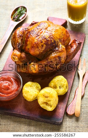 Roast Chicken on wooden board with potatoes and ketchup, photographed with natural light (Selective Focus, Focus in the middle of the image)