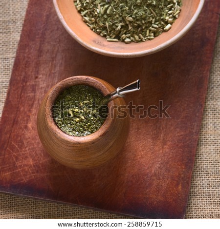 South American yerba mate tea in wooden mate cup with strainer called bombilla, photographed with natural light. Mate is the national infusion of Argentina (Selective Focus, Focus on the tea in cup)