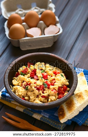 Scrambled eggs with red bell pepper and green onion in rustic bowl, toasted bread on the side, eggs in back, photographed with natural light (Selective Focus, Focus one third into the scrambled eggs)