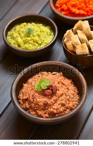 Homemade red kidney bean spread with kidney beans and fresh coriander leaf, zucchini-parsley spread and bread in back, photographed with natural light (Selective Focus, Focus on the coriander leaf)