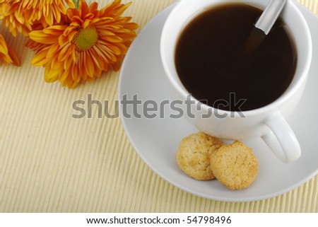 Black tea in cup with saucer, teaspoon, biscuits and orange flower in the background on table mat photographed from top (Selective Focus)