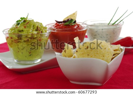 Tacos in bowl with three different dips (guacamole, tomato-chili dip and cream cheese dip) in the background on red tablecloth on white (Selective Focus)
