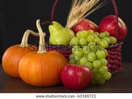 An autumn basket with apple, pear, grapes, wheat and pumpkins (Selective Focus, Focus on apple and pumpkin in front)