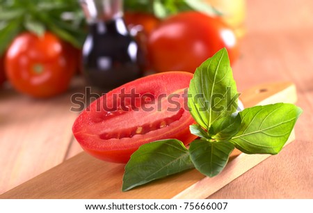 Fresh basil leaves with tomato halves with tomato and balsamic vinegar in the back (Selective Focus, Focus on the leaves on top and the right)