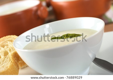 Cream of asparagus with a green asparagus head on top in a white bowl with baguette slices beside (Very Shallow Depth of Field, Focus on the asparagus head in the soup)