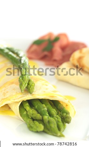Green asparagus wrapped in crepes with Hollandaise sauce and green asparagus as garnish on top (Selective Focus, Focus on the asparagus heads on top of the crepes)