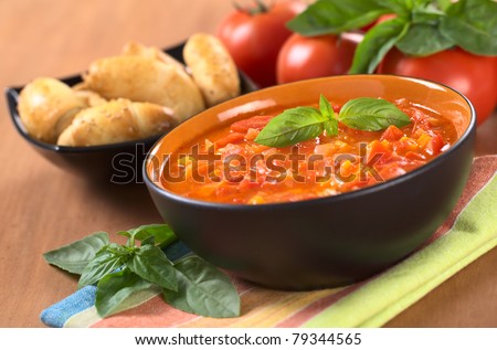 Chunky tomato soup made of tomatoes, carrots and onions and garnished with a basil leaf (Selective Focus, Focus on the basil leaf on the soup)