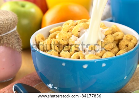 Pouring milk over a bowl full of honey flavored cereal loops (Selective Focus, Focus on the milk stream)