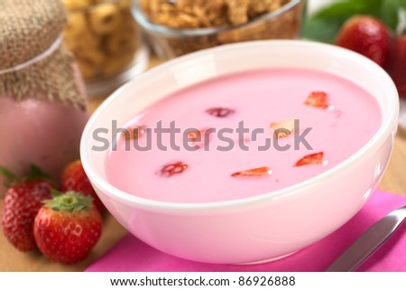 Fresh strawberry yogurt with strawberry pieces with strawberries, cereals and yogurt in glass around (Selective Focus, Focus on the strawberry pieces in the front in the yogurt)