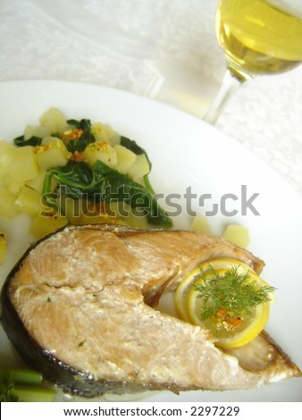 Delicious salmon steak dinner served with olive oil dressing and accompanied with cooked potato and spinach.