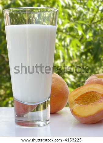 Glass of milk and a couple of peaches on a white table. Blurred scenery of the countryside in the background.