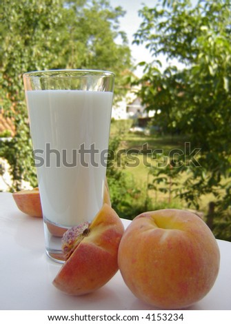 Glass of milk and a couple of peaches on a white table. Blurred scenery of the countryside in the background.