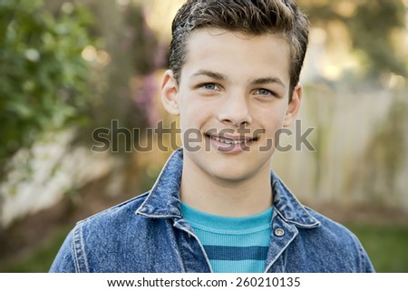 Smiling teenage boy outside, wearing denim jacket, horizontal format, 13 yrs old