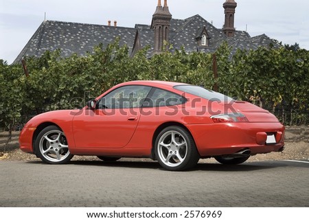 red sports car , parked next to vineyards, large  house in the background
