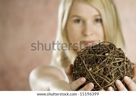 blond female with arms extended holding a ball made of tree branches, ball is focus point