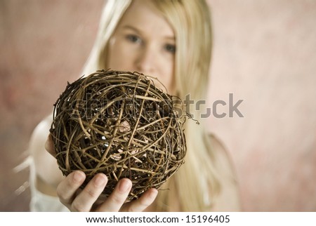 blond female with arms extended holding a ball made of tree branches, ball is focus point