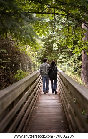 man and woman taking a walk in the woods, on a wooden bridge