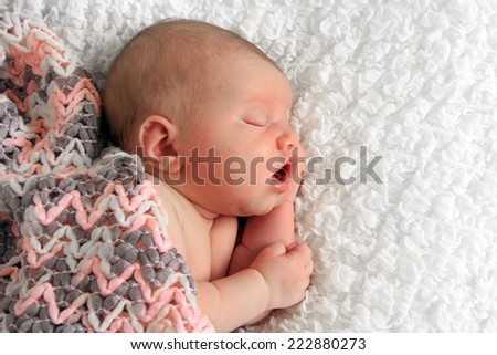 Newborn baby girl asleep on a white blanket.