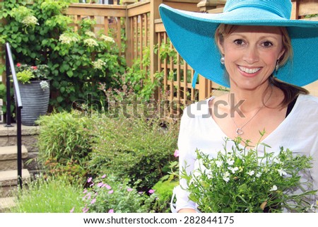 Smiling fifty year old lady gardener outside in the garden holding a pack of lobelia.