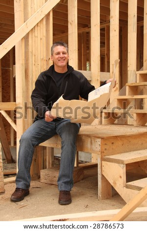 Builder with blue prints in a house under construction.
