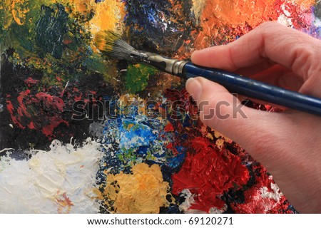 Hand holding a paintbrush on an abstract oil painting. Focus on brush and painting, not on the hand.