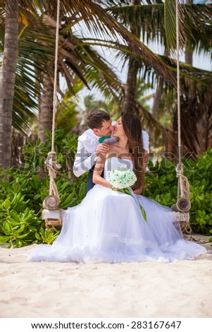 young loving couple on their wedding day, on the swing, outdoor beach wedding in tropics