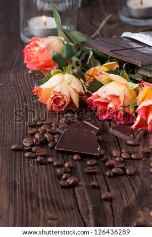 Bunch of orange roses with dark chocolate and coffee beans on old wooden table