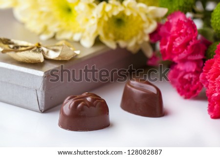 Black and white chocolate candies and bouquet of carnation and chrysanthemum flowers over white