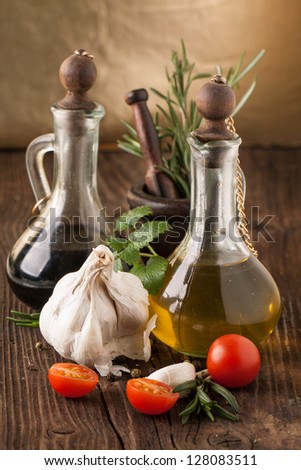 olive oil and vinegar in vintage bottles on wooden table, sliced tomatoes cherry with garlic, mint and rosemary in wooden mortar