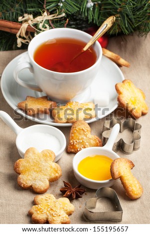 Cup of black tea served with homemade Christmas sugar cookies, honey and metal cookie cutters over tablecloth