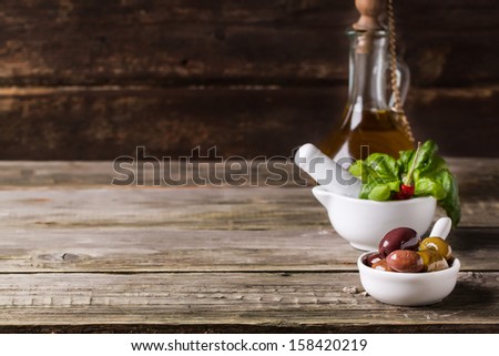Wooden background with mix of olives with fresh basil in white mortar and vintage bottle of olive oil on old wood