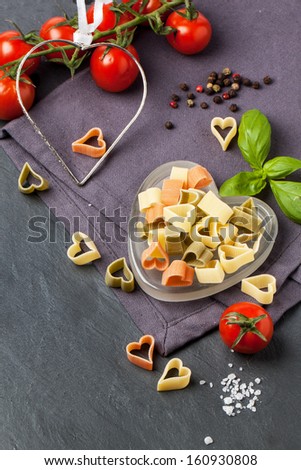 Dry colorful pasta as heart shape with fresh tomatoes and basil served on dark gray background