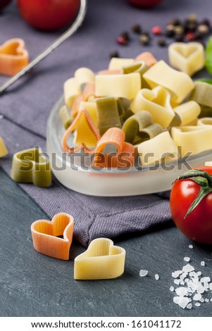 Close up of dry colorful pasta as heart shape with fresh tomatoes and basil served on dark gray background