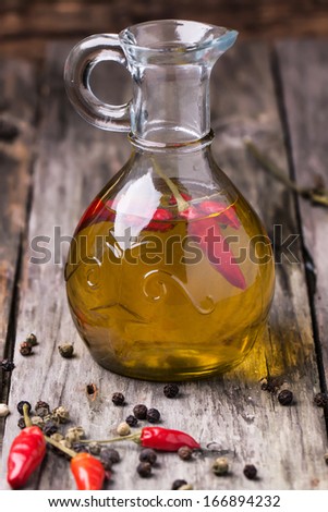 Glass bottle of olive oil with red hot chili peppers over old wooden background. See series