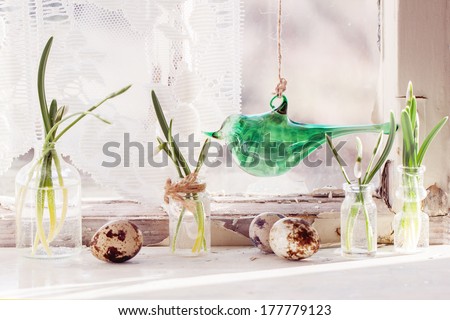 Fragment of Easter interior on old windowsill with little glass vials, blossom snowdrops,  glass bird and quail eggs. See series