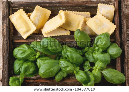 Top view on wooden box with homemade pasta ravioli with fresh basil on old wooden table.