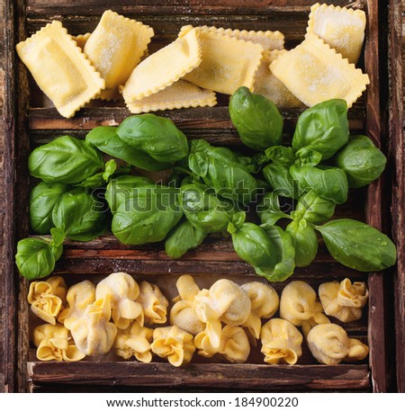 Top view on wooden box with homemade pasta ravioli and perle with fresh basil on old wooden table.