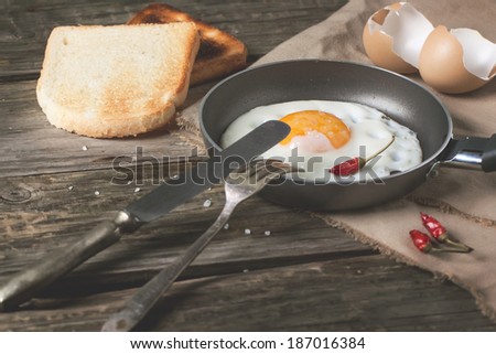 Breakfast with fried egg on pan served with toasts, red hot chili peppers and vintage tableware over old wooden table